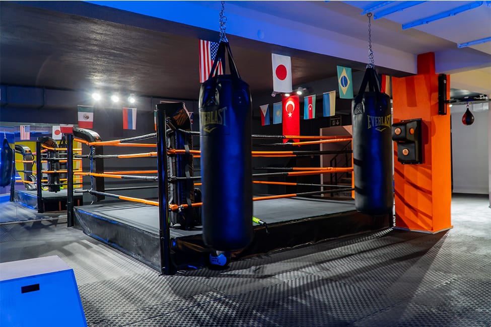 Today Living Club boks ringi: turuncu halatlar, tavandan sarkan Everlast kum torbaları ve turuncu sütunda vuruş pedi