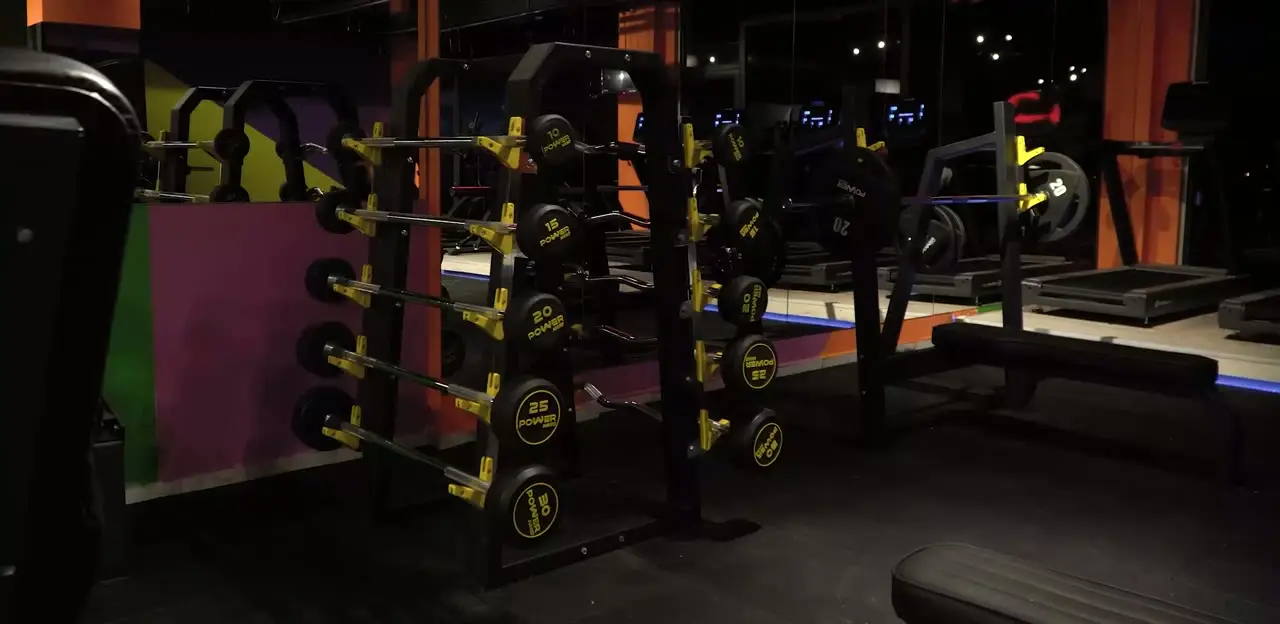 Akşam ışığında fitness katı: ağırlık istasyonları, turuncu kolonlar ve mavi LED hattı